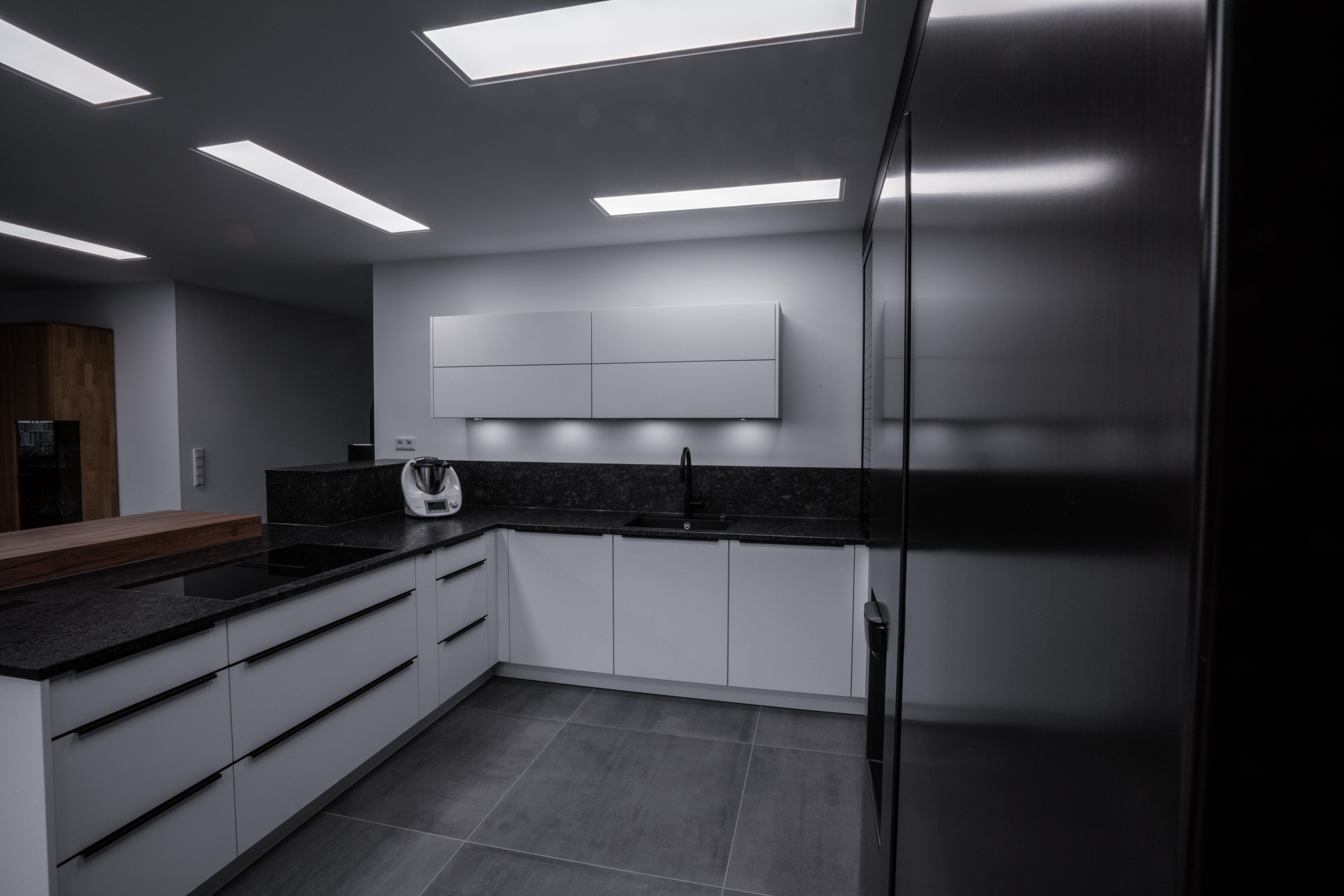 Moderne, minimalistische Küche in Weiß und Schwarz mit glatten Oberflächen und Induktionskochfeld.