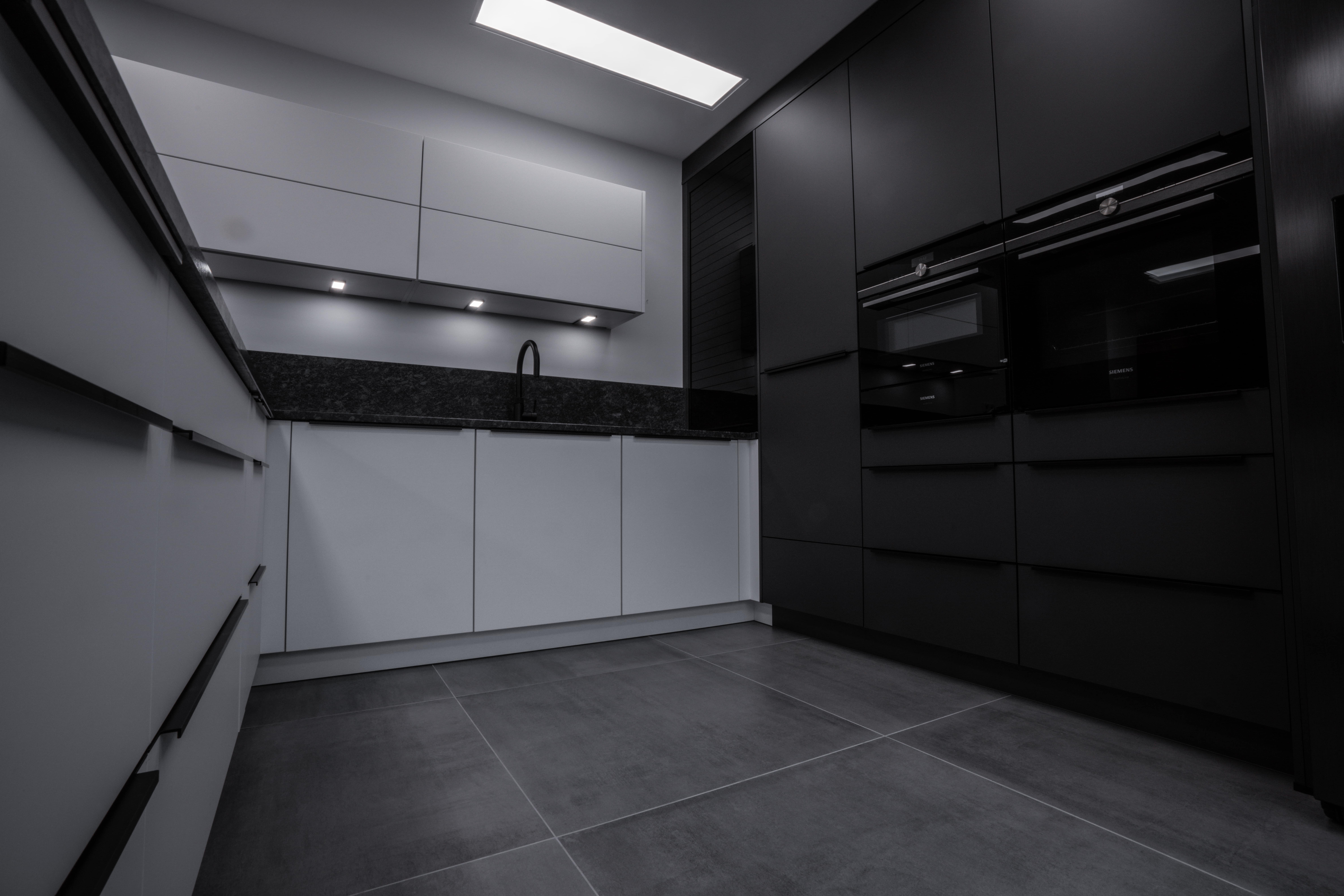 Moderne, minimalistische Küche in Schwarz-Weiß mit integrierten Geräten und dunkler Arbeitsplatte.