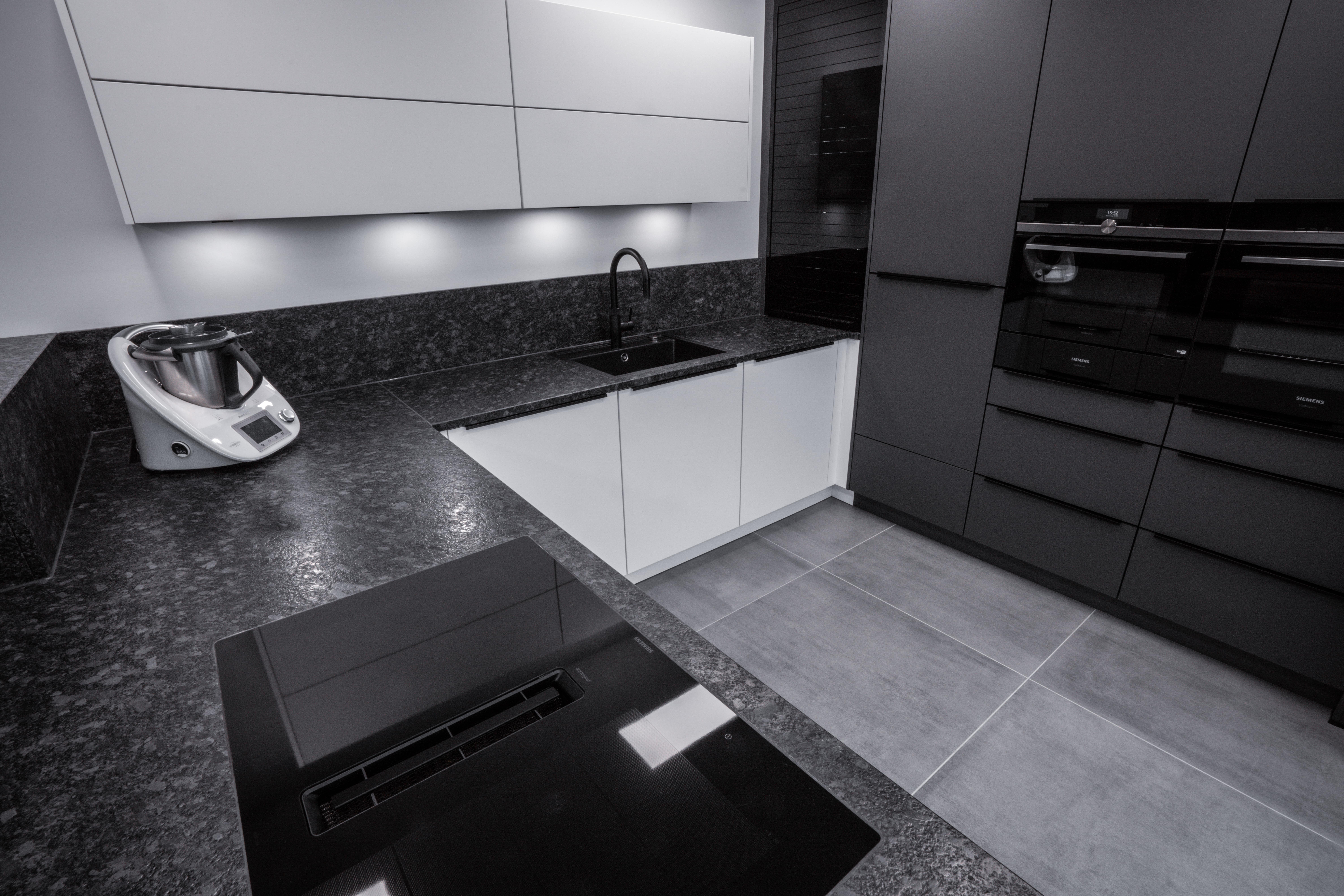 Moderne Küche in Schwarz-Weiß mit Mixer, schwarzem Kochfeld und eleganter Beleuchtung.