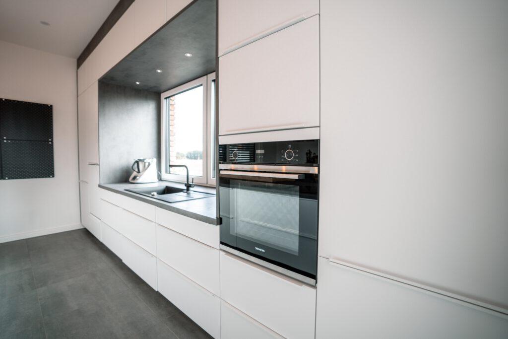 Moderne, minimalistische Küche mit weißen Schränken, schwarzem Backofen und Küchenroboter auf Arbeitsplatte.