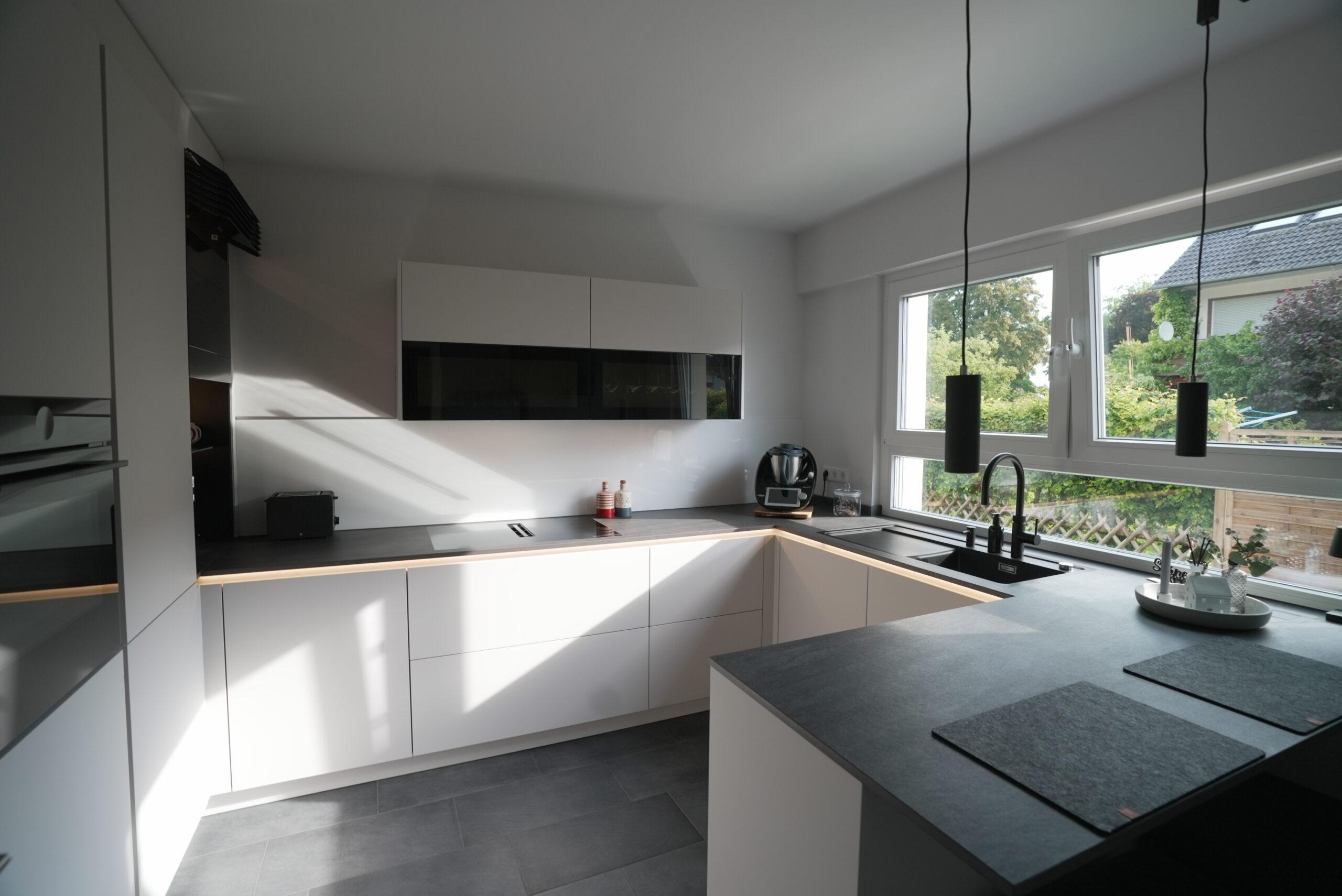 Moderne, minimalistische Küche mit weißen Schränken, dunkler Arbeitsplatte und natürlichem Licht.