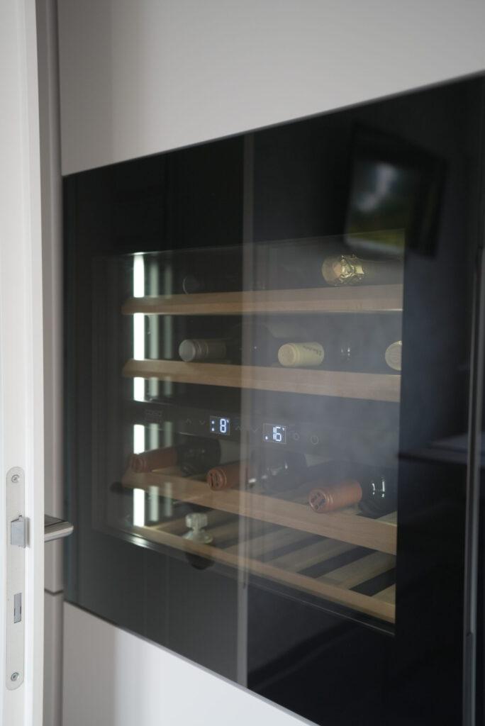 Moderner Weinkühlschrank mit Glastür, zeigt Weinflaschen auf hölzernen Regalen in eleganter Umgebung.