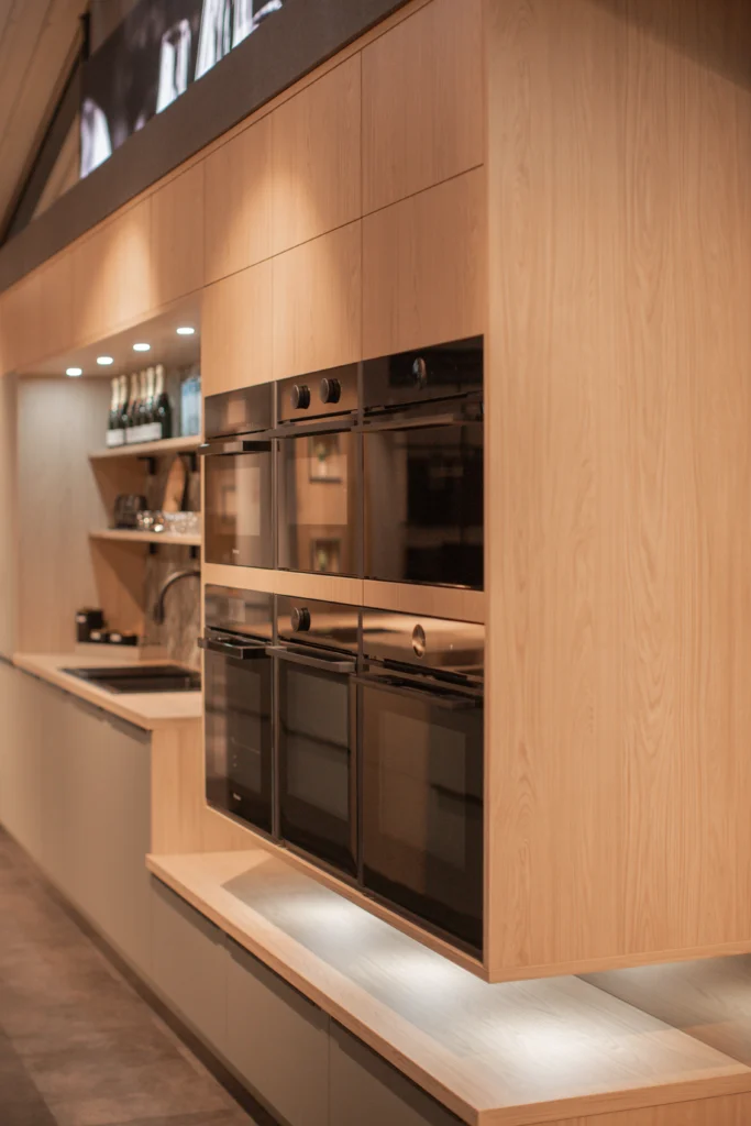 Moderne Küche mit Holz- und Schwarztönen, eingebauten Öfen und offenen Regalen. Keine Personen sichtbar.