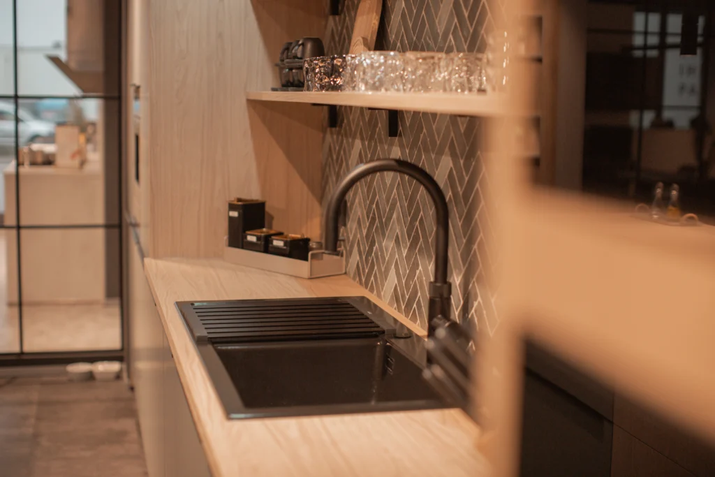 Moderne Küche mit Holzarbeitsplatte, Waschbecken, Regal mit Gläsern und Fischgrätenmuster-Fliesen.