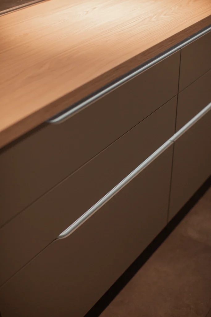 Moderne Küchenzeile mit grauen Schubladen und heller Holzarbeitsplatte, minimalistisch und elegant.