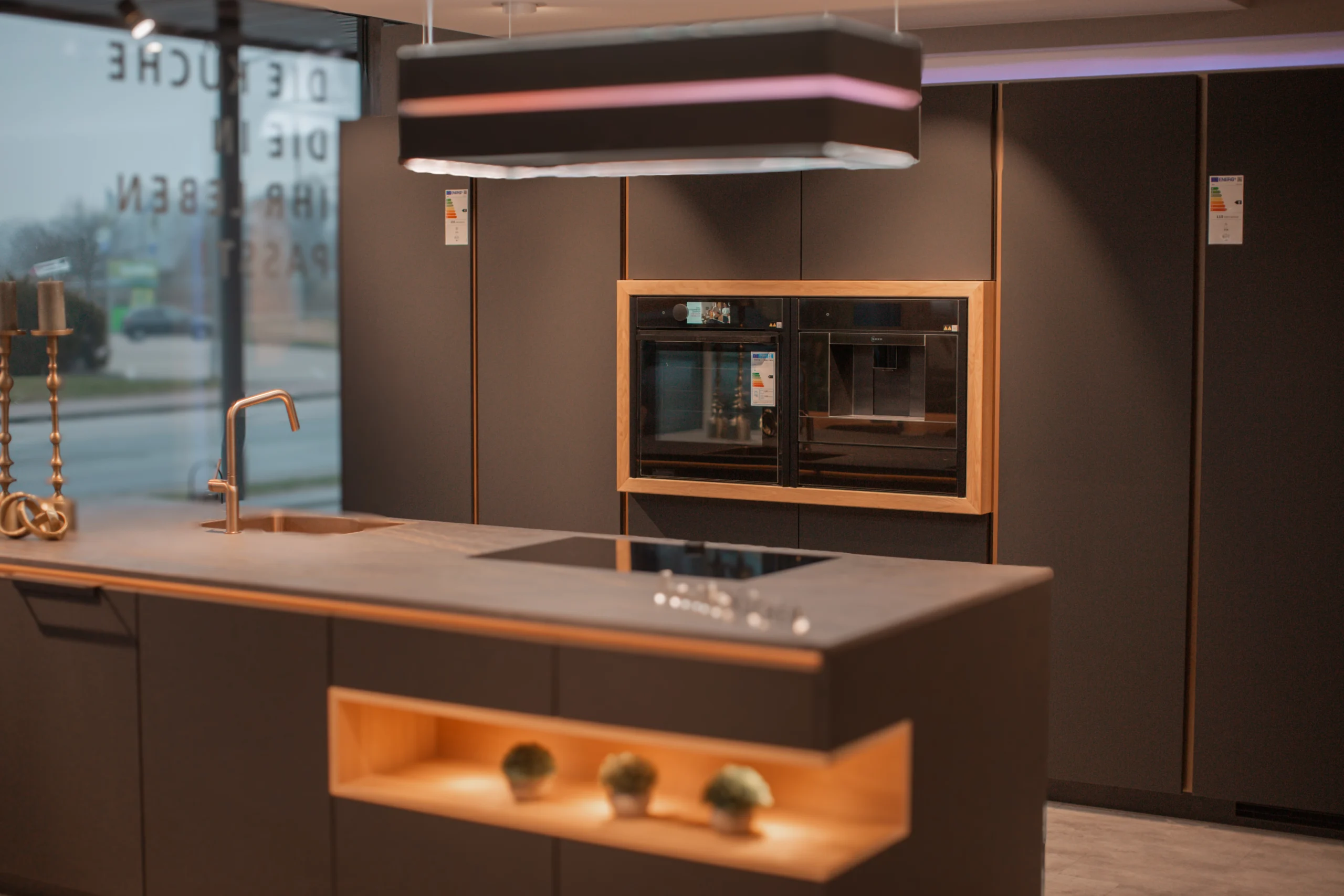 Moderne, aufgeräumte Küche mit dunklen Farben, Holzakzenten und eleganter Beleuchtung über der Insel.