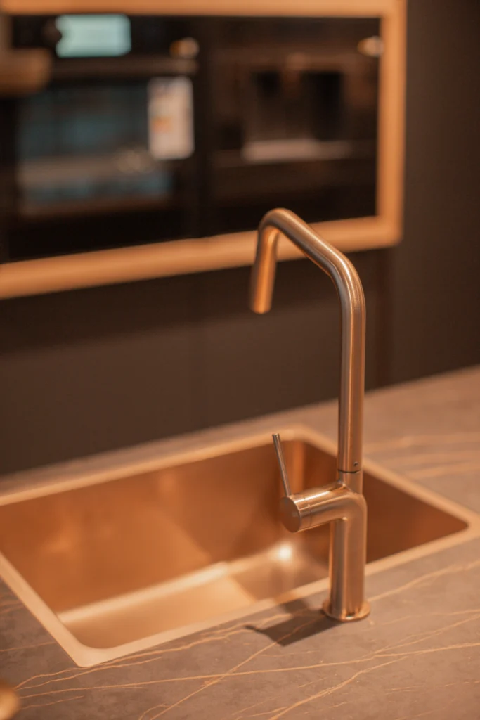 Moderne bronzefarbene Küchenspüle mit passendem Wasserhahn, auf dunkler, marmorierter Arbeitsplatte.