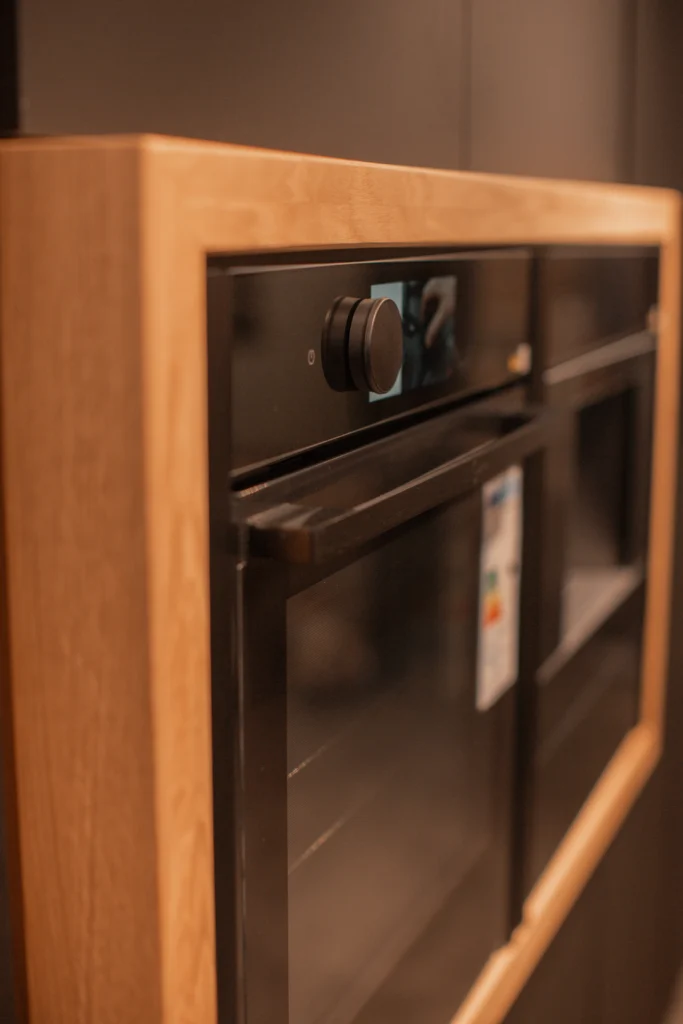 Moderner schwarzer Einbauofen mit großem Drehknopf, umrahmt von hellem Holz in einer eleganten Küche.