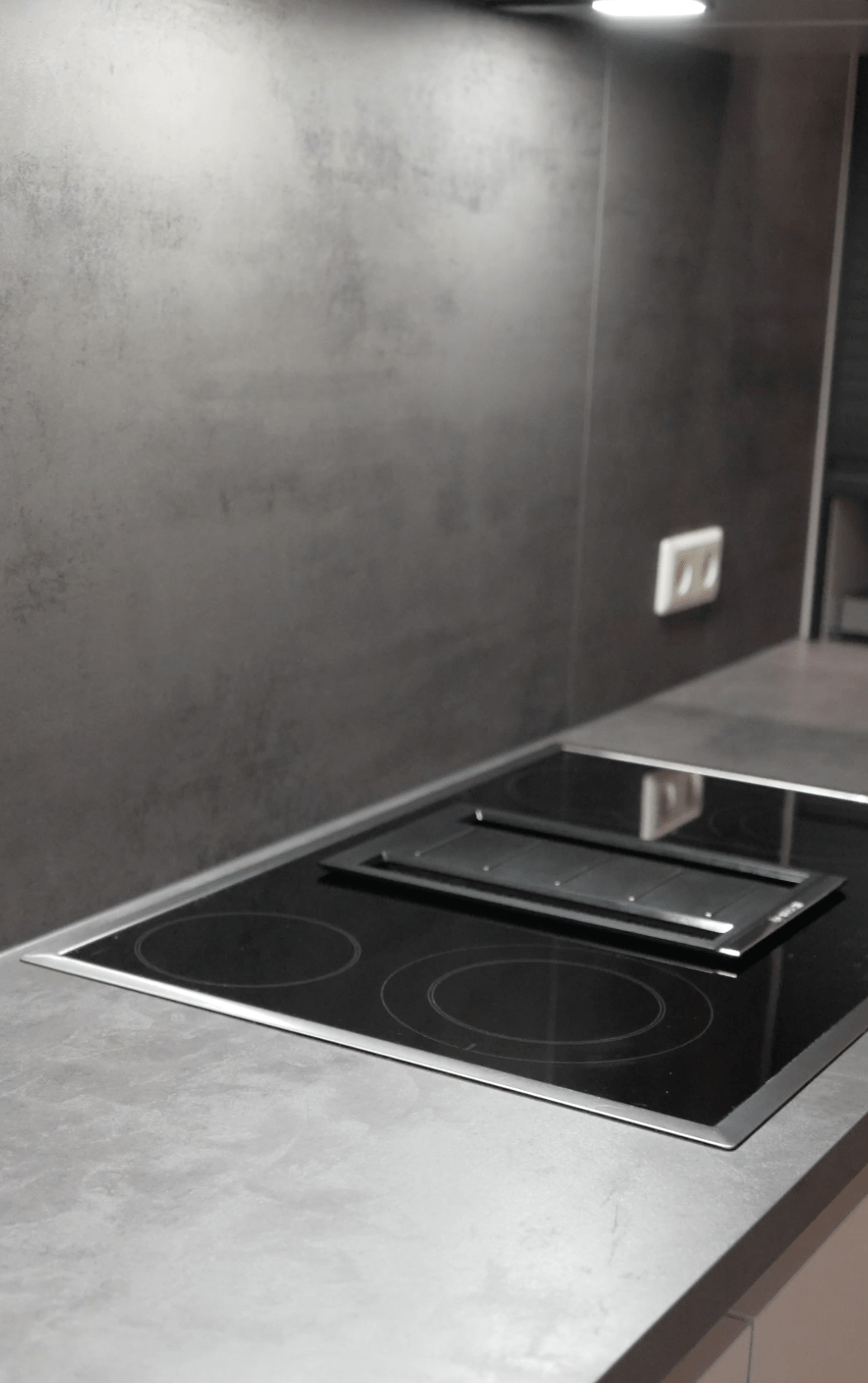 Moderne Küche mit schwarzem Induktionskochfeld und grauer Arbeitsplatte, minimalistisch gestaltet.
