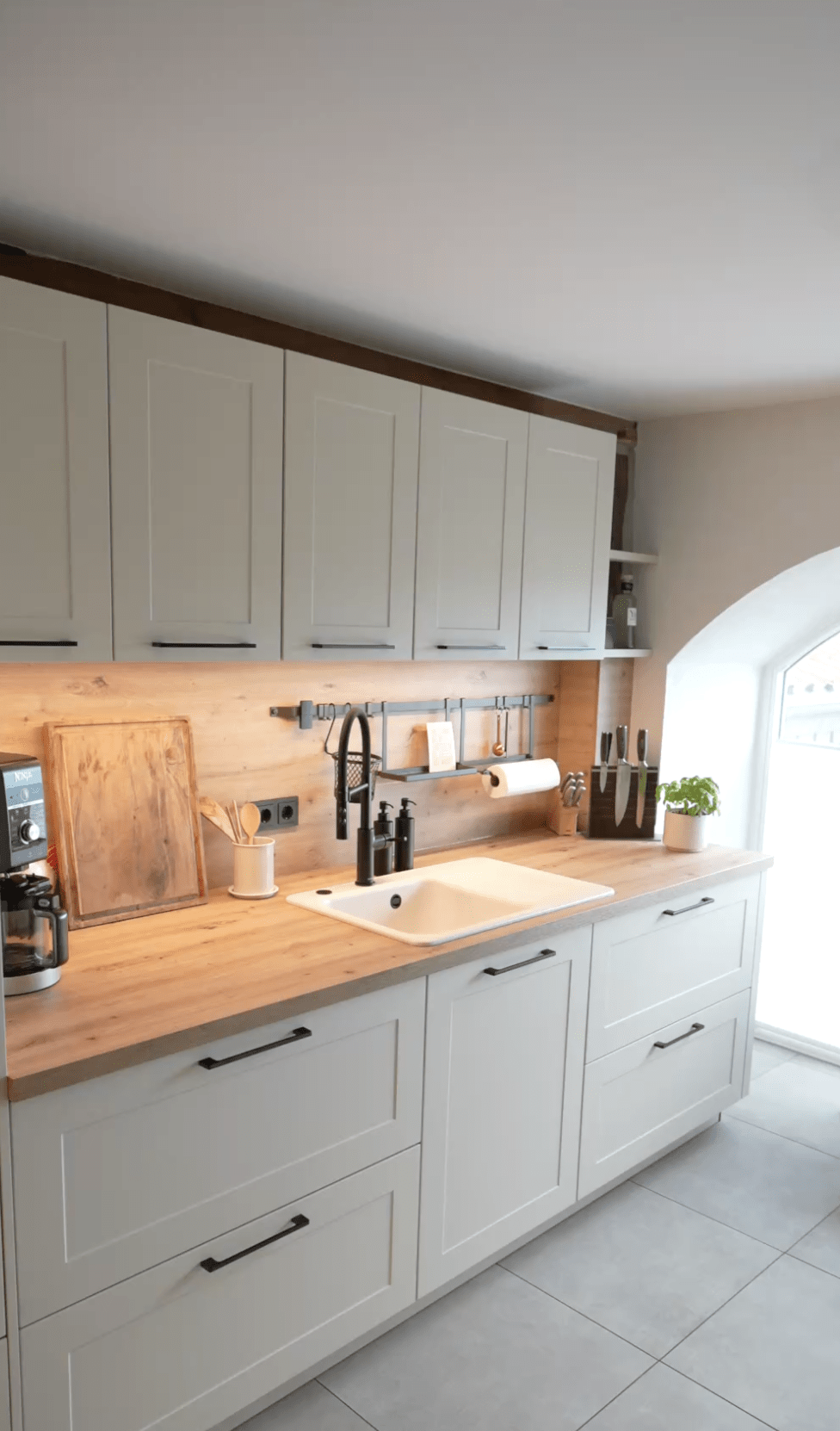 Moderne Küche mit weißen Schränken, Holzelementen, Kaffeemaschine und Basilikumtopf.