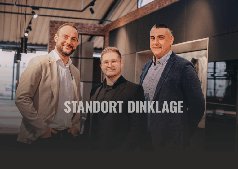 Drei Männer in Anzügen lächeln in einem modernen Büro, der Text "STANDORT DINKLAGE" ist sichtbar.