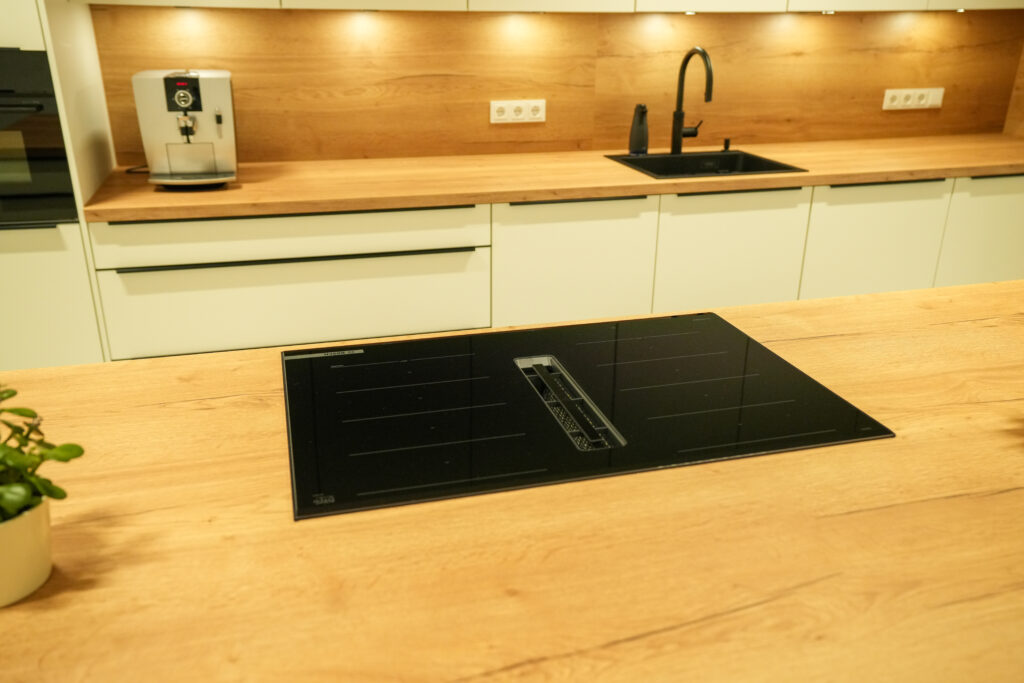 Moderne Küche mit Holzarbeitsplatten, Induktionskochplatte, Spüle, Kaffeemaschine und Pflanzentopf.