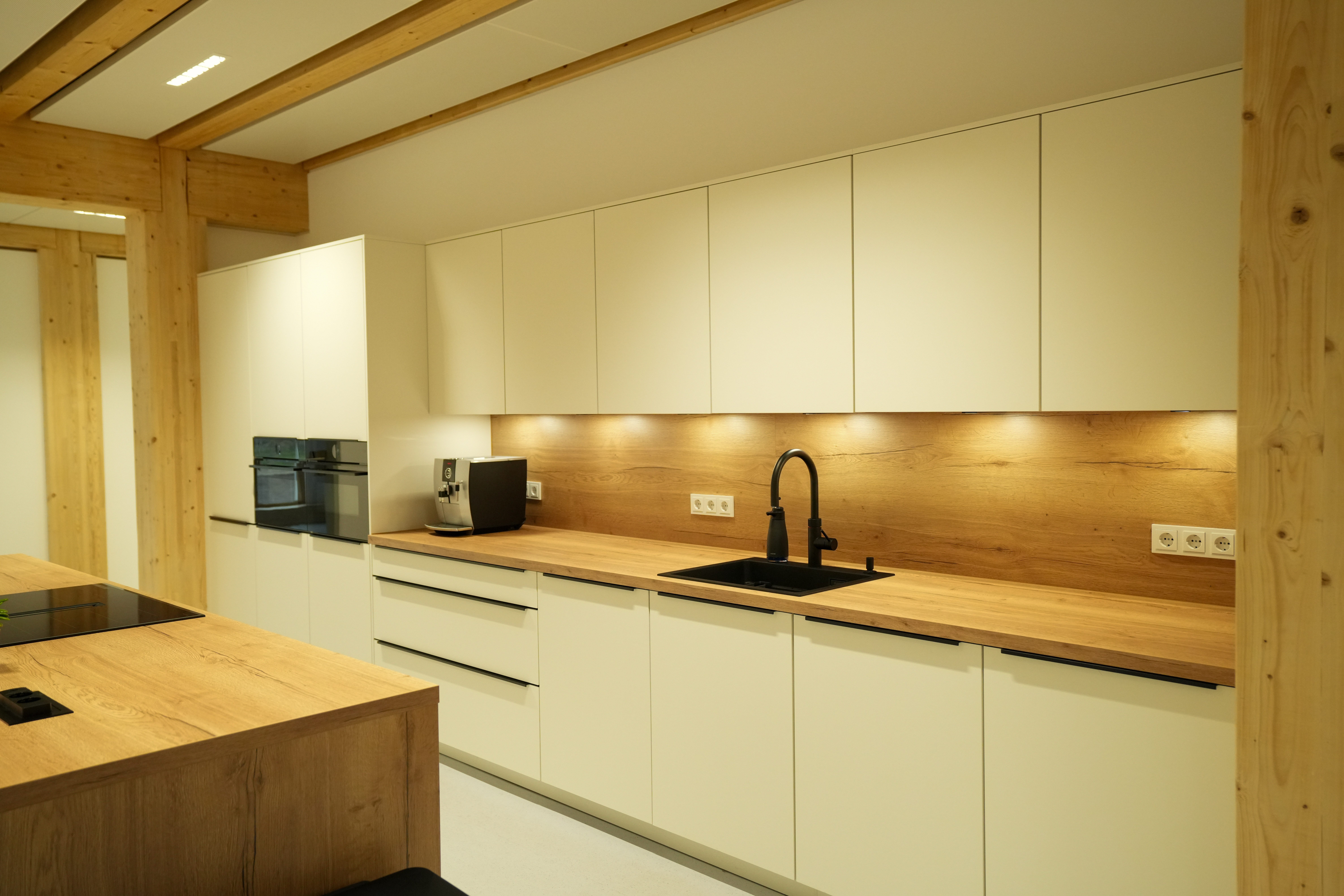 Moderne Küche mit weißen Schränken, Holzarbeitsplatte, schwarzem Waschbecken und warmem Licht.