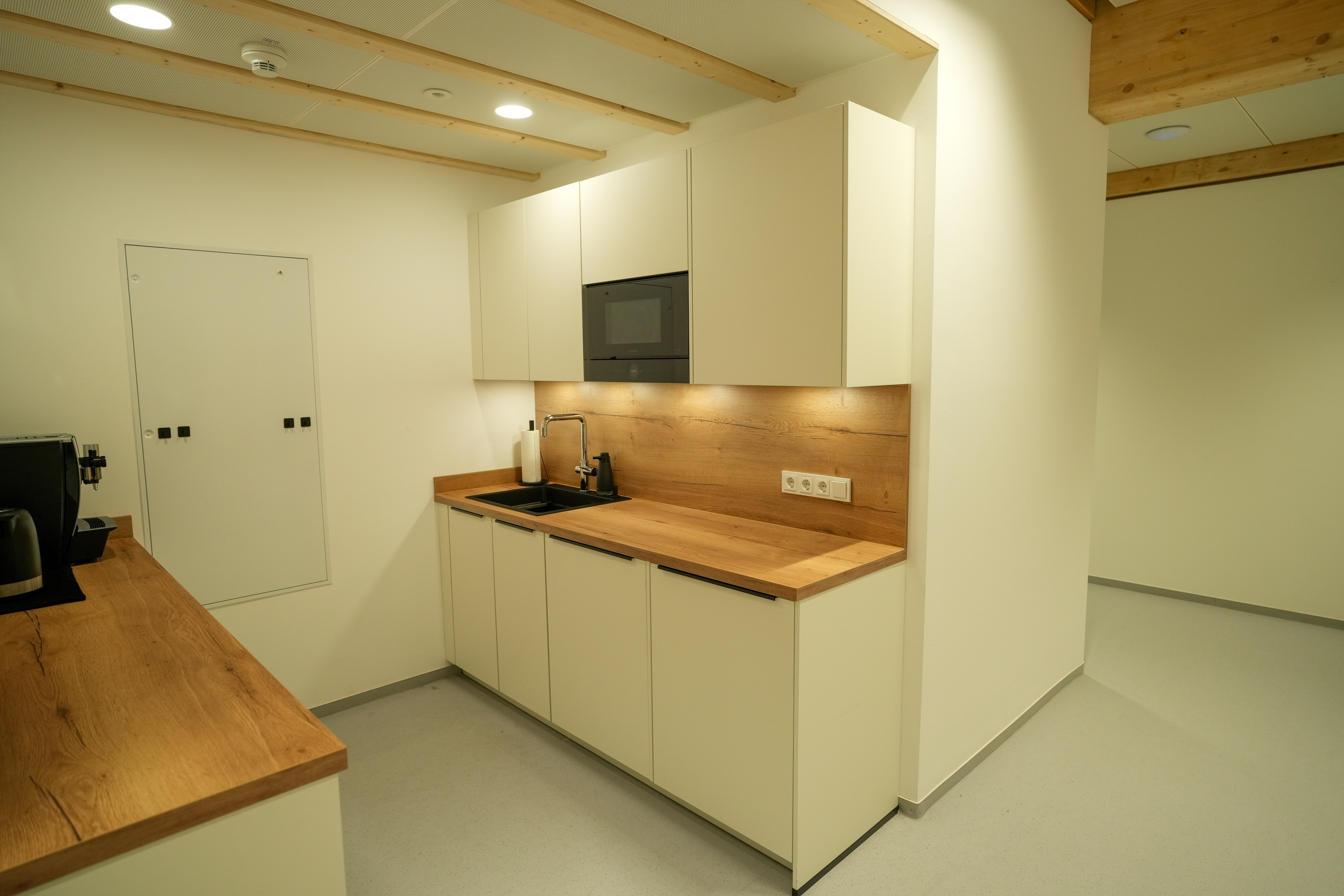 Moderne, minimalistische Küche mit weißem Block, Holzarbeitsplatte, Waschbecken und Kaffeemaschine.