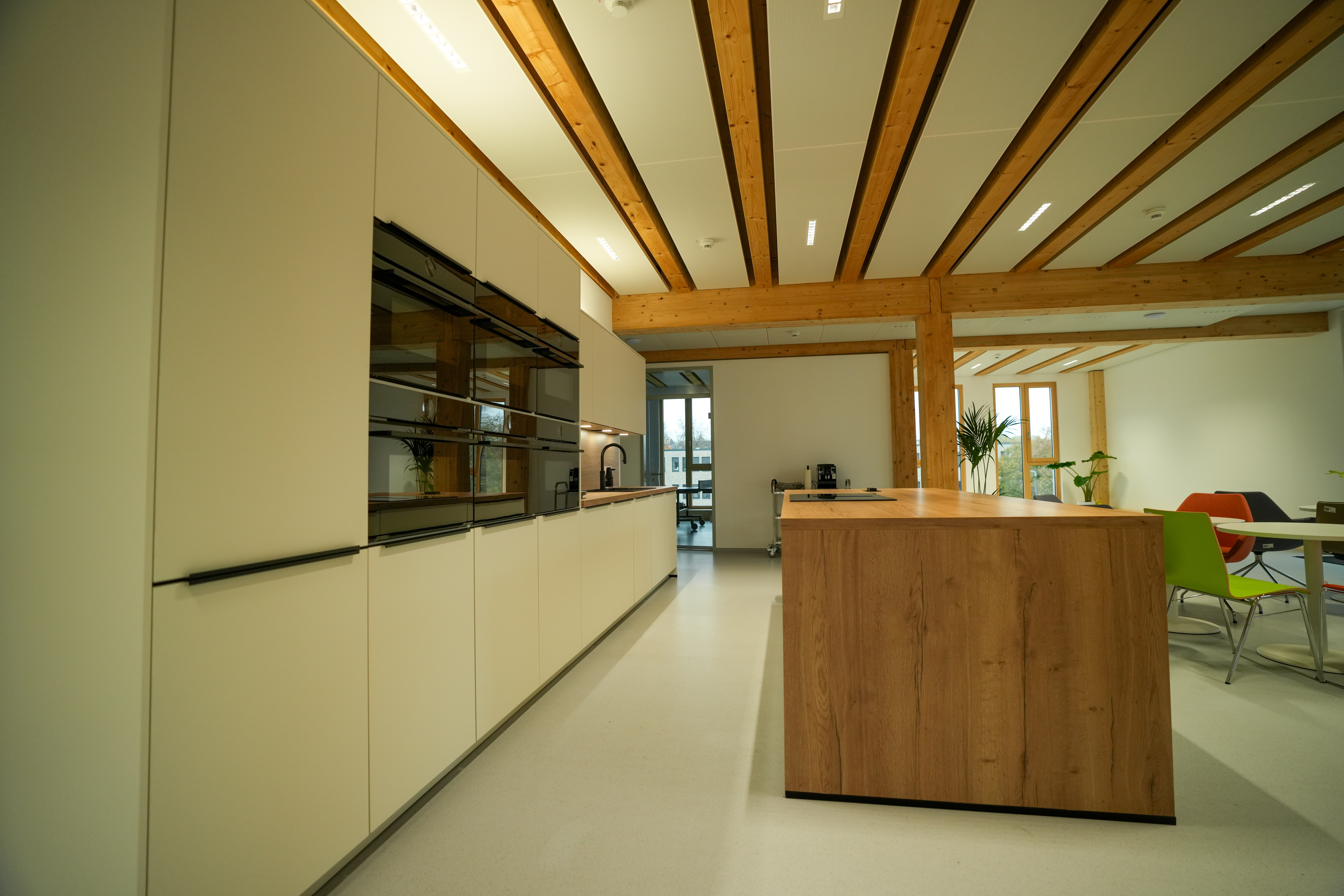 Moderne Küche mit Holzinsel, bunten Stühlen und Pflanzen, in einem offenen, einladenden Raum.