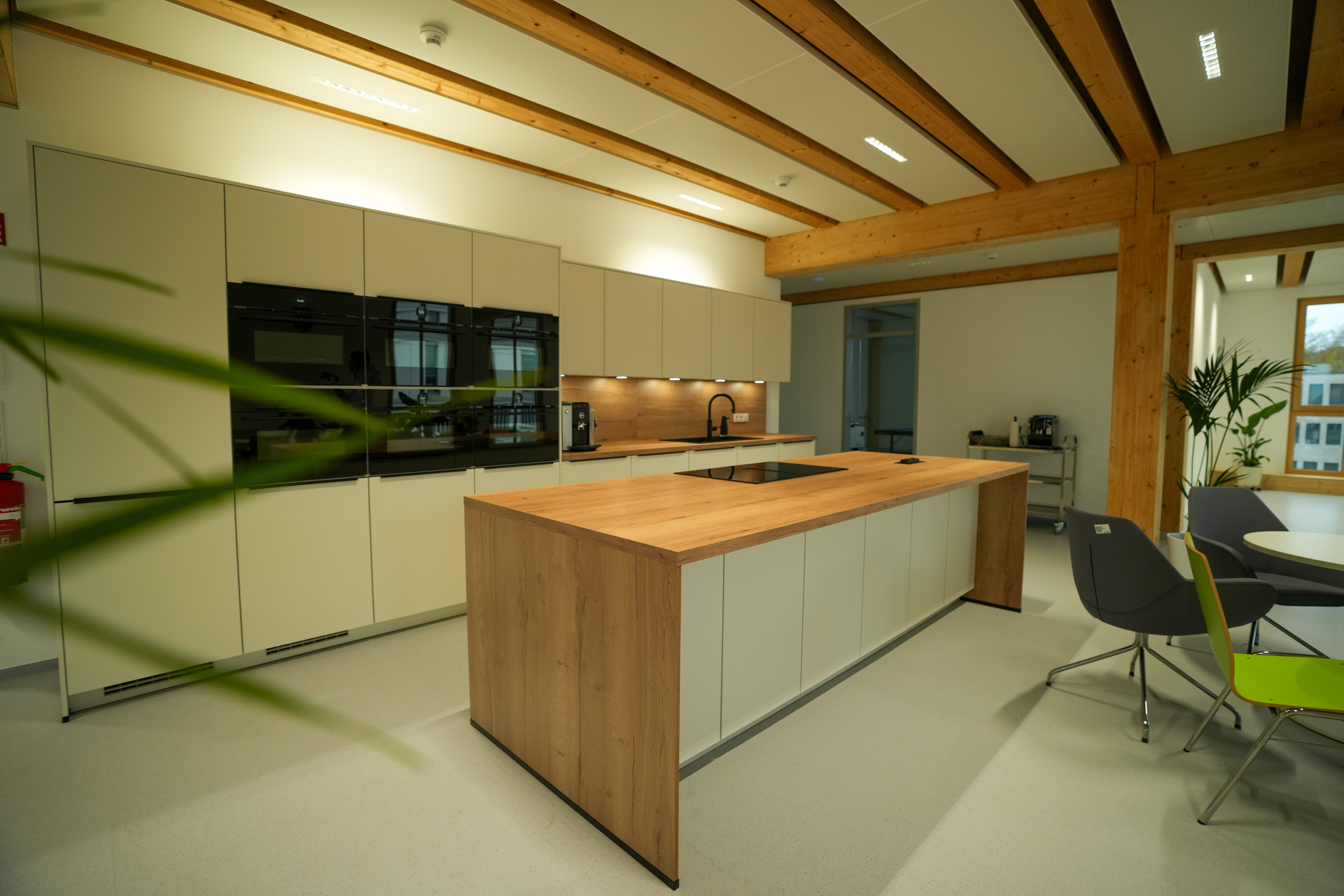 Moderne Küche mit heller Holzarbeitsplatte, weißen Schränken und farbigen Stühlen, einladend gestaltet.