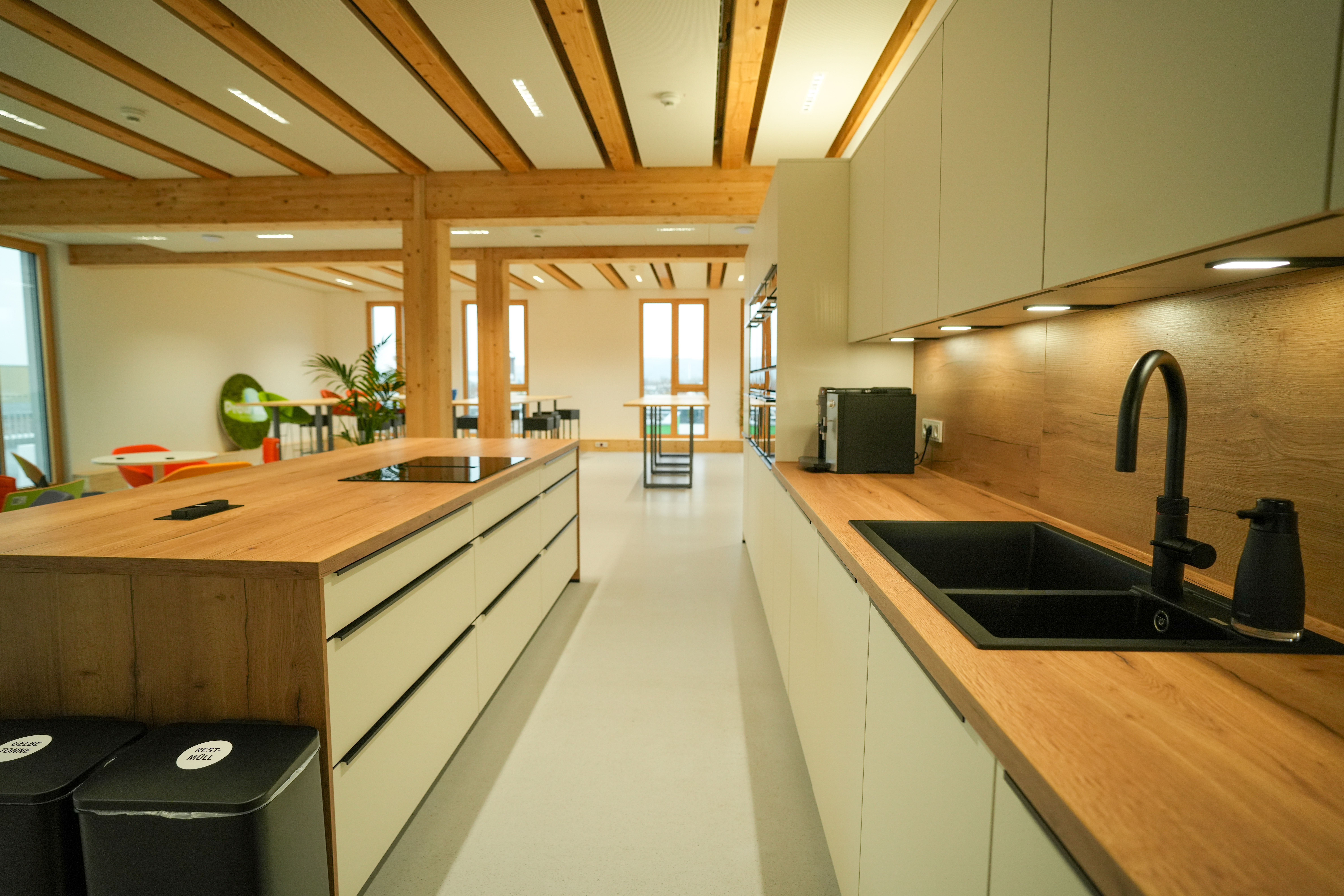 Moderne Küche mit Holz- und Beigetönen, Kücheninsel, Mülltrennung und Essbereich im Hintergrund.