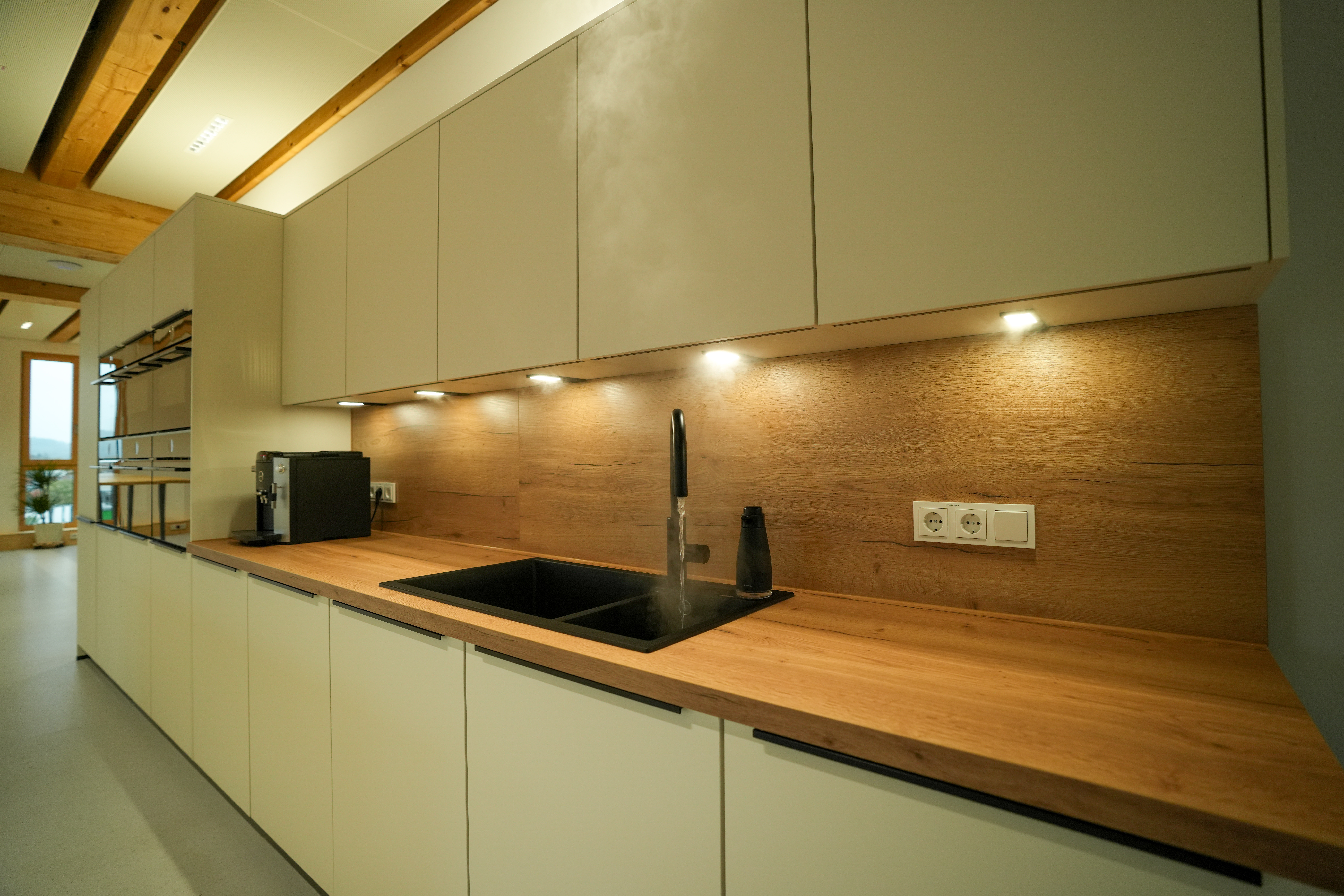 Moderne Küche mit Holzarbeitsplatte, heißem Wasser im schwarzen Spülbecken und Kaffeevollautomat.