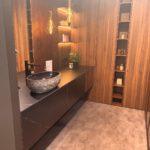 Modernes Badezimmer mit rundem Steinwaschbecken, dunklem Waschtisch und warmen Holztönen.