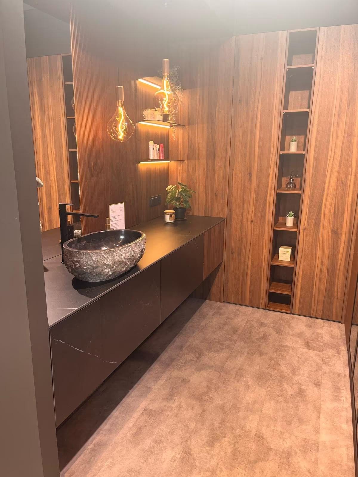 Modernes Badezimmer mit rundem Steinwaschbecken, dunklem Waschtisch und warmen Holztönen.