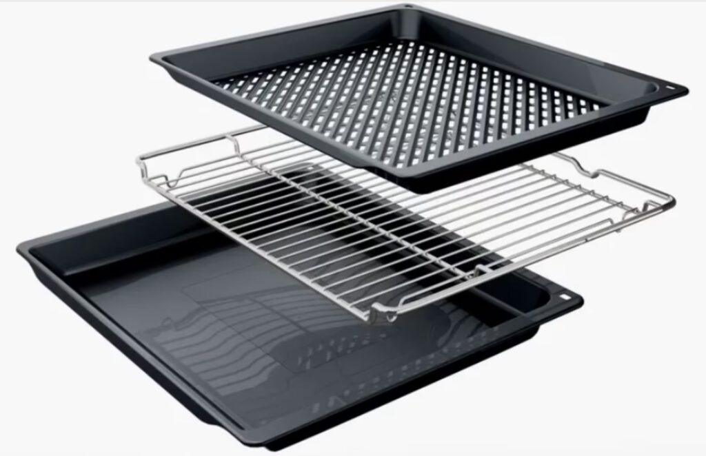 Drei gestapelte Küchenutensilien: gelochtes Backblech, Gitterrost und flaches Backblech in dunklen Tönen.