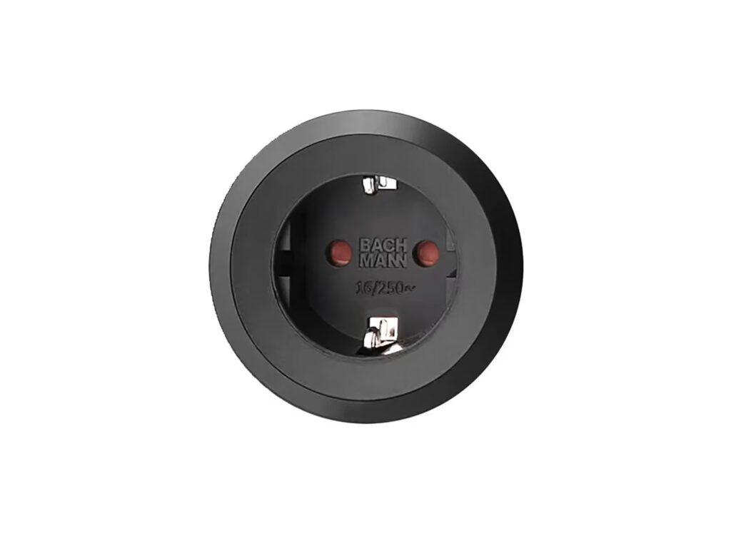 Runde, schwarze Steckdose mit zwei Öffnungen und Schutzkontakt, roter Punkt als Sicherheitsmerkmal.