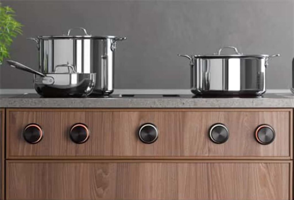 Moderne Küche mit glänzenden Edelstahltöpfen auf einem eleganten Kochfeld mit schwarzen Drehknöpfen.