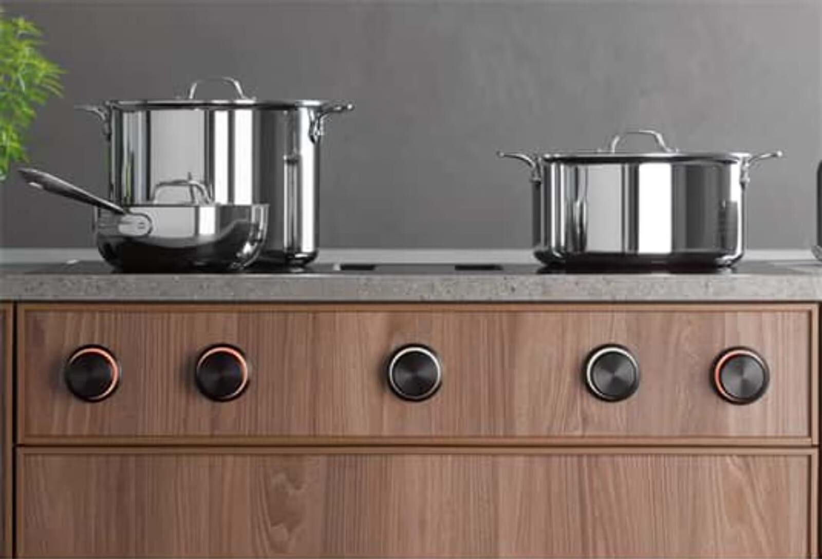 Moderne Küche mit glänzenden Edelstahltöpfen auf einem eleganten Kochfeld mit schwarzen Drehknöpfen.