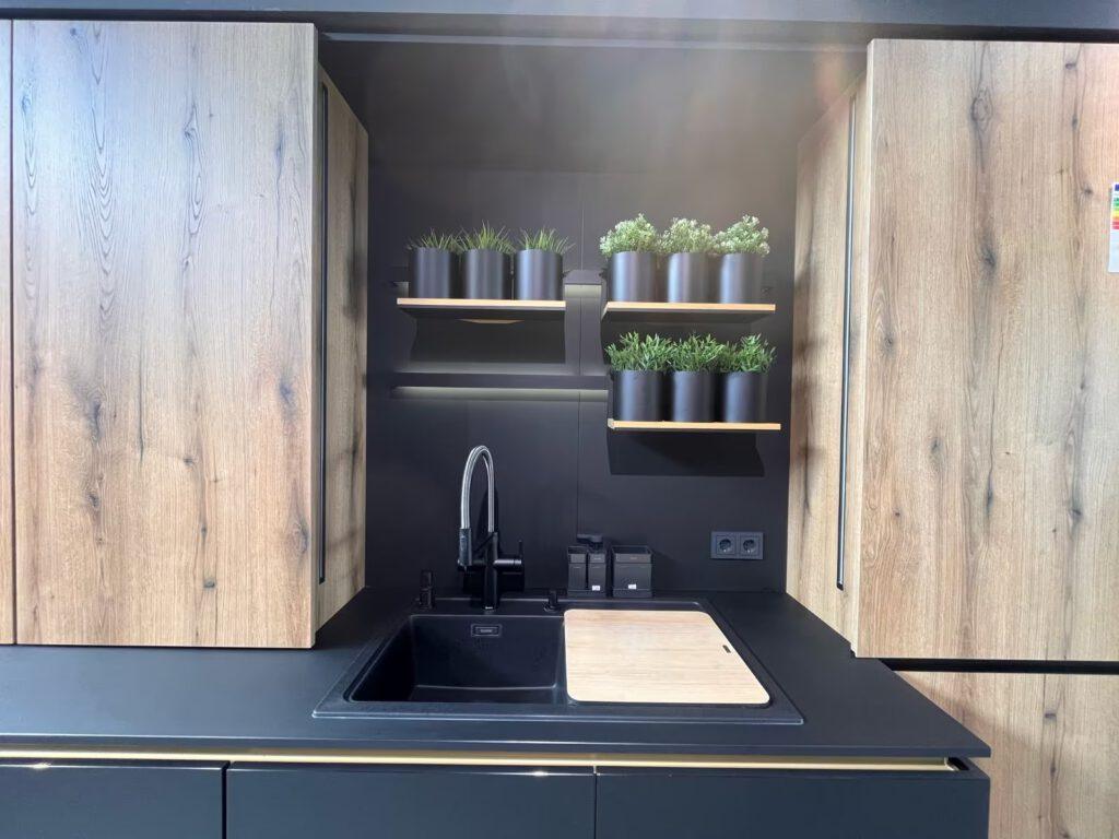 Moderne Küche mit schwarzer Spüle, Holzschränken und grünen Pflanzen auf Regalen.