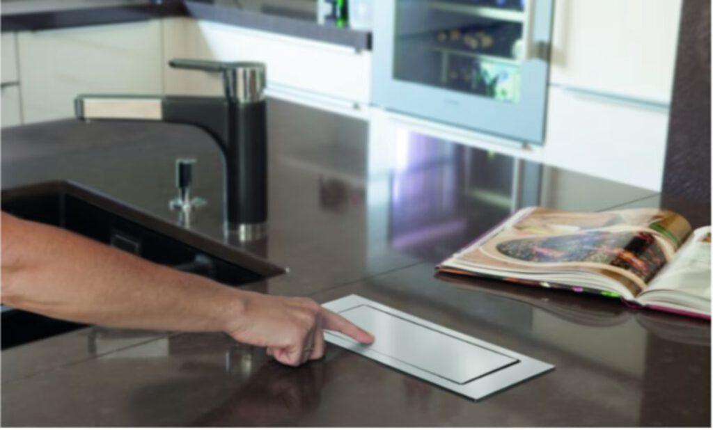 Eine Hand bedient ein Touch-Bedienfeld in einer modernen Küche mit Wasserhahn und offenem Buch.