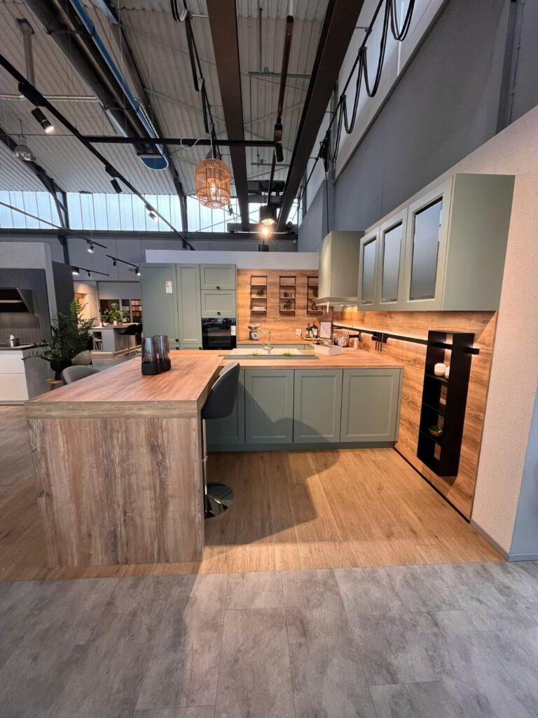 Moderne Ausstellungsküche mit grünen Schränken, Holzarbeitsplatte und Barhockern in gemütlicher Atmosphäre.