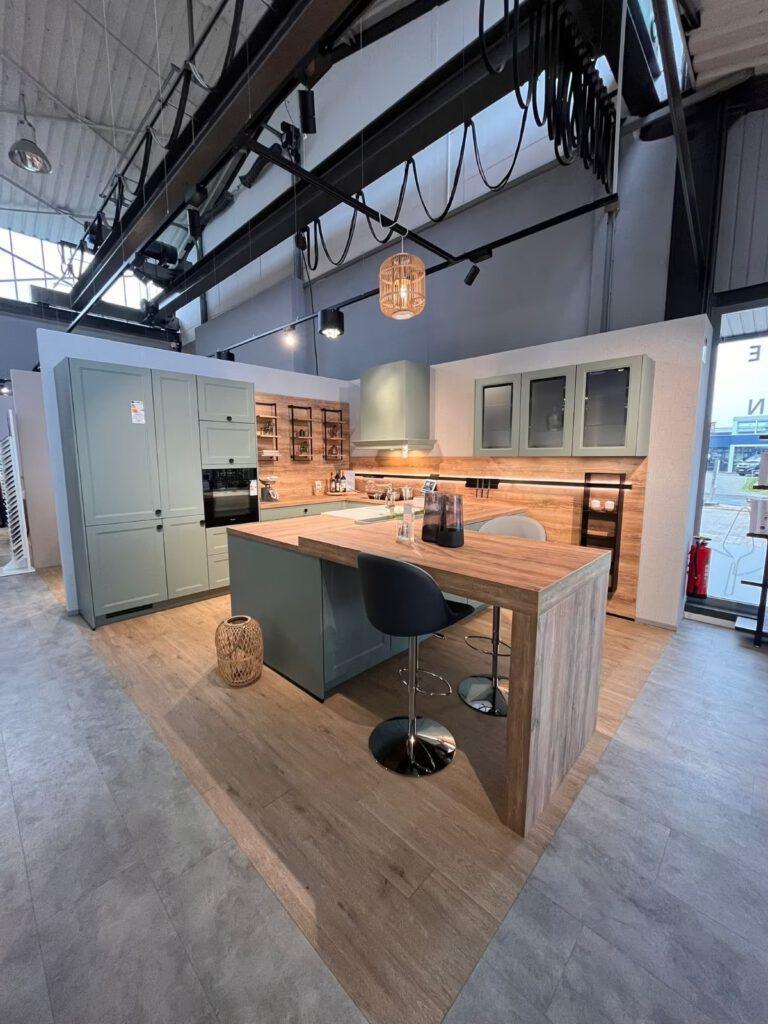 Moderne Küchenzeile mit grauen Schränken, Holzinsel und Barhockern in einem Ausstellungsraum.