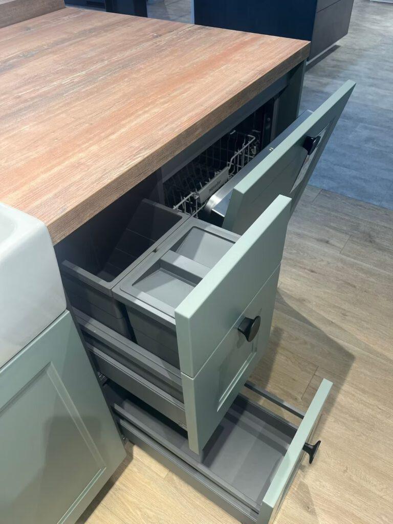 Geöffnete mintgrüne Küchenschubladen und Spülmaschine auf Holzarbeitsplatte in moderner Küche.