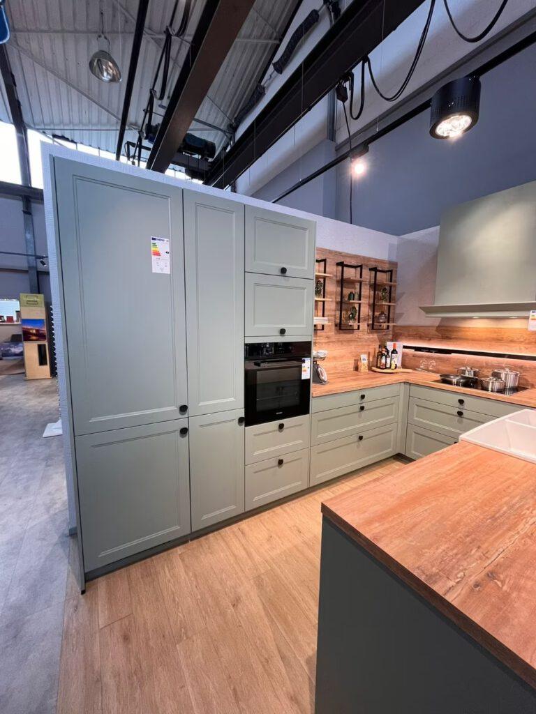 Moderne Ausstellungsküche mit grünen Einbauschränken, Holzarbeitsplatte und eingebautem Backofen.