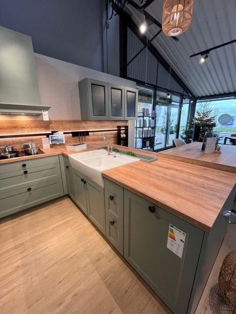 Moderne Ausstellungsküche mit grünen Schränken, Holzarbeitsplatte und warmem, einladendem Licht.