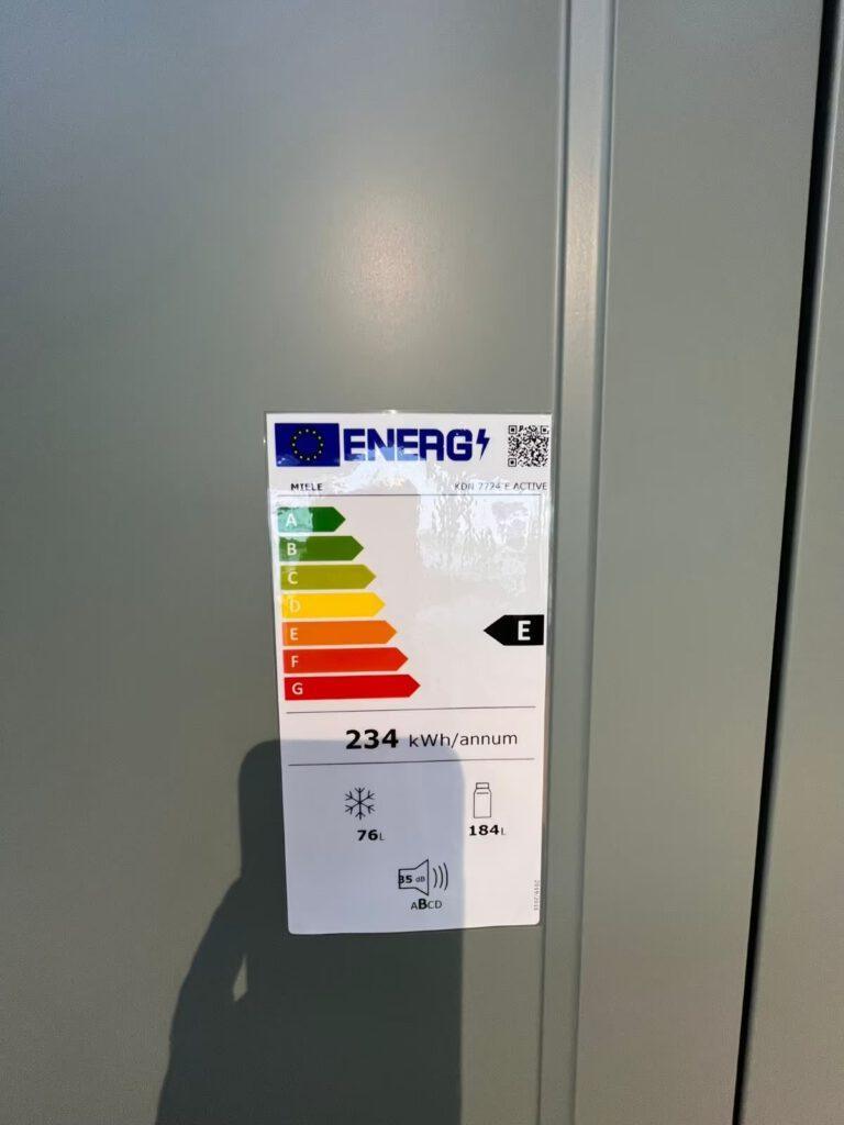Energielabel auf grauer Oberfläche zeigt Klasse E, 234 kWh Verbrauch, 76L Gefrierfach, 184L Kühlfach.
