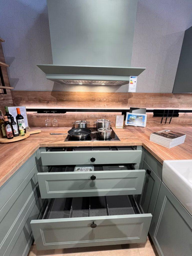 Moderne Küche mit grünen Schränken, Holzarbeitsplatte, Kochfeld, Spüle und Gewürzen auf Drehteller.