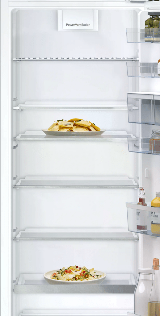 Ein geöffneter Kühlschrank zeigt Teller mit Ravioli und Salat sowie Flaschen in der Tür.