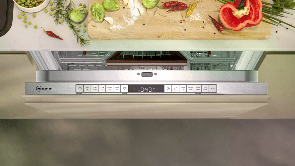 Offene Neff-Geschirrspülmaschine in moderner Küche, Schneidebrett mit buntem Gemüse auf Arbeitsfläche.