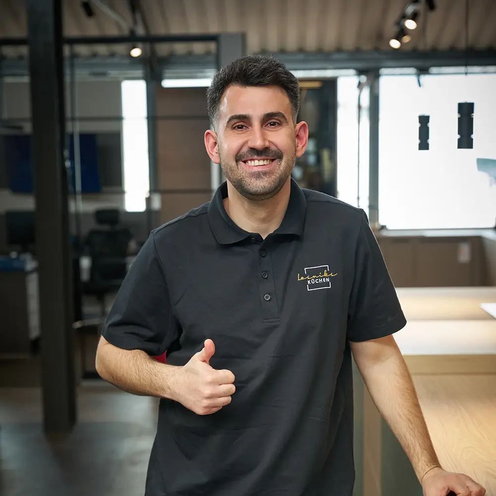 Ein Mann in schwarzem Poloshirt lächelt und zeigt Daumen hoch in einem modernen Büro.