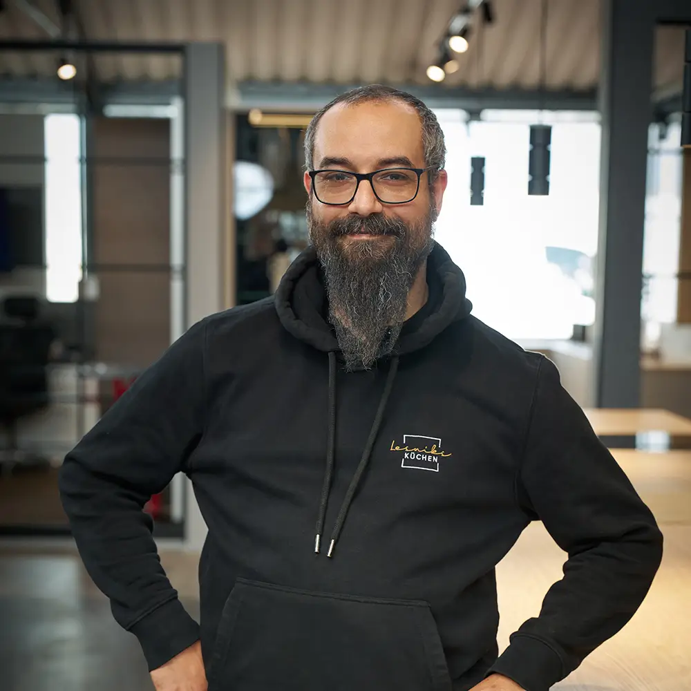 Eine Person mit Brille und Bart lächelt in einem modernen, gut beleuchteten Raum in die Kamera.