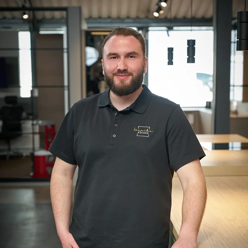 Ein lächelnder Mann im schwarzen Poloshirt steht in einem modernen, industriellen Innenraum.