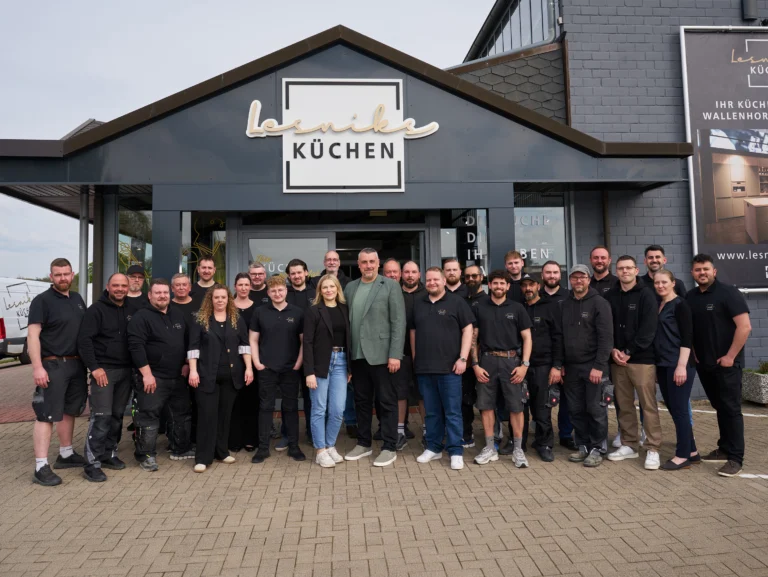 Eine Gruppe von etwa 20 Personen posiert lächelnd vor einem Gebäude mit dem Schild "Lesnik Küchen".