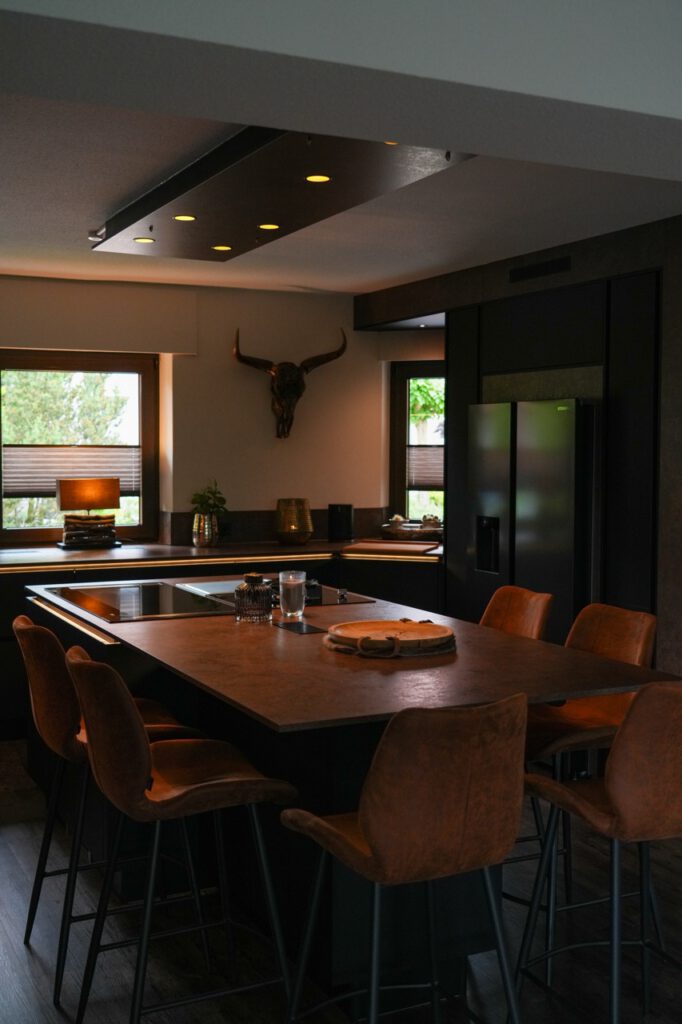 Moderne Küche mit dunkler Insel, braunen Barhockern, dekorativem Stierkopf und schwarzem Kühlschrank.