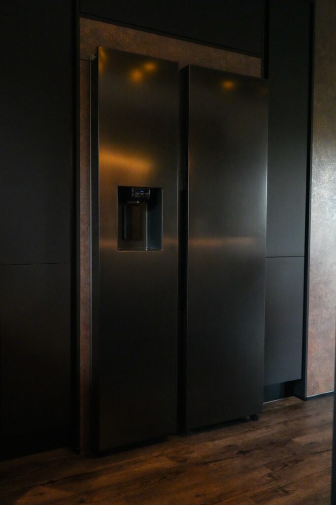Moderner schwarzer Kühlschrank mit Wasserspender, in eleganter Küche mit Holzfußboden und dunklen Wänden.