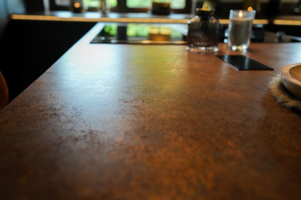 Gemütliche Küche mit Glasflasche, brennender Kerze und Holztablett auf rostfarbener Arbeitsfläche.