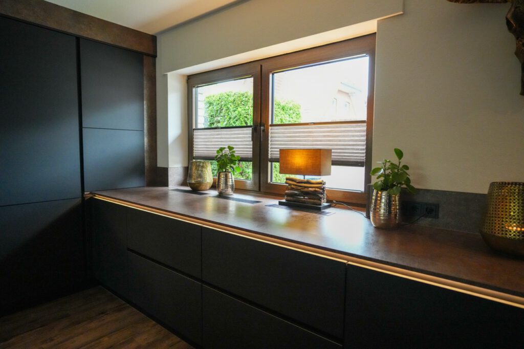 Moderner Innenraum mit dunklen Schränken, warm beleuchteter Lampe, Pflanzen und goldener Vase.