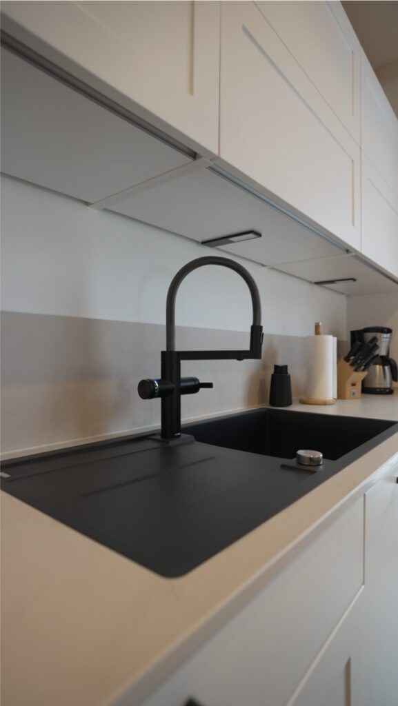 Moderne Küche mit schwarzem Spülbecken, weißen Schränken und minimalistischer Einrichtung.