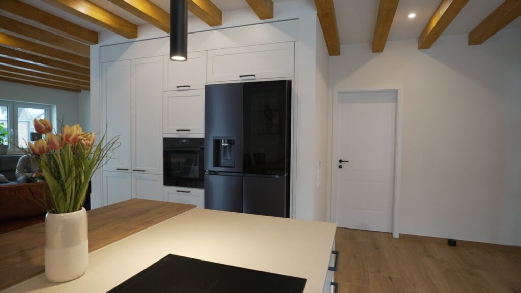 Moderne Küche mit schwarzem Kühlschrank, Kochinsel, Backofen und Vase mit bunten Tulpen.