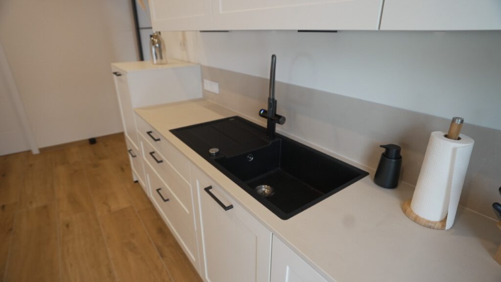 Moderne Küche mit schwarzer Spüle, weißen Schränken und minimalistischer Dekoration.
